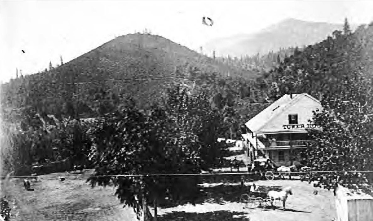 Historic photo of Tower House and surroundings, a two-story structure in a mountain area beside mature trees, grazing animals.