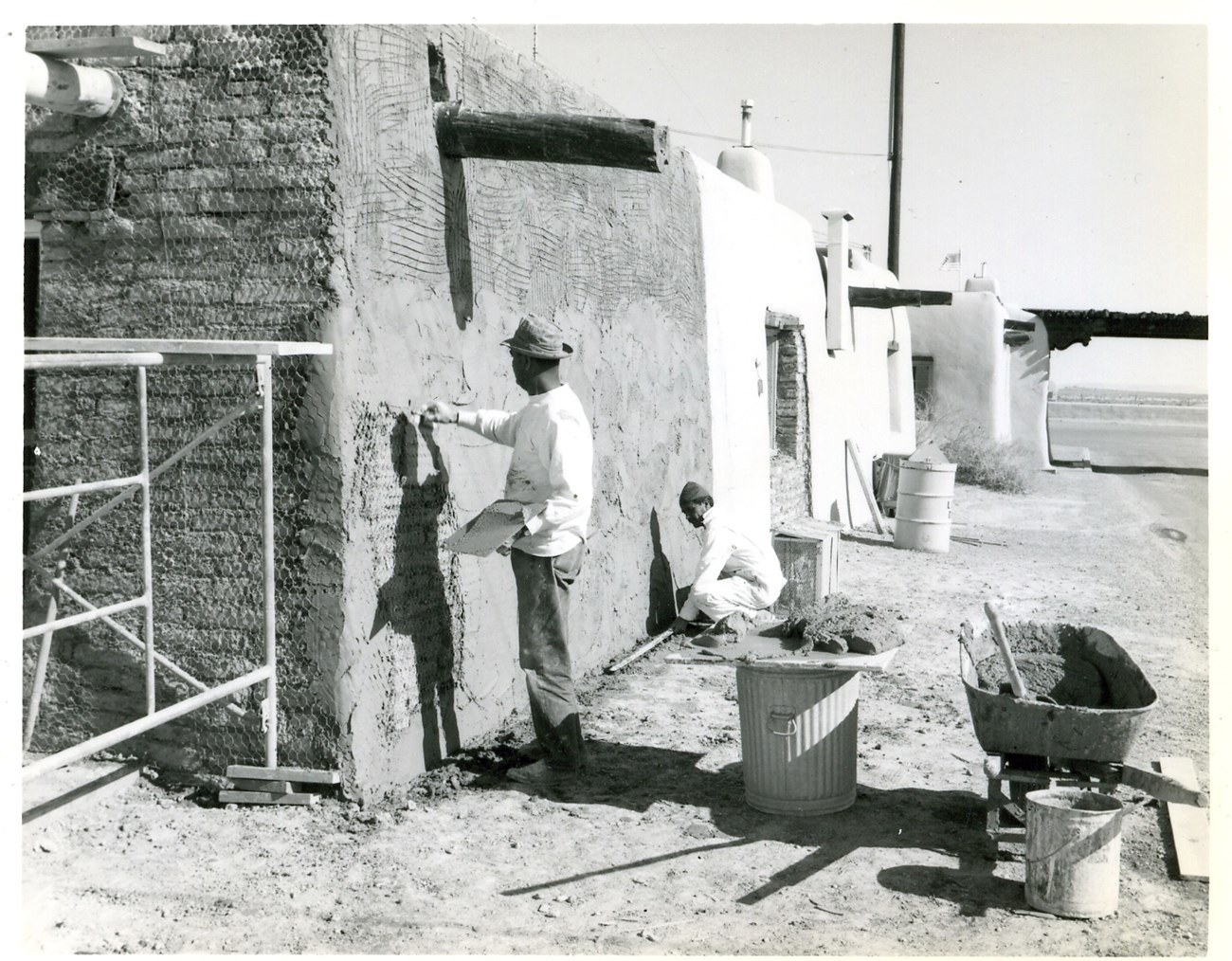 WHSA Visitor Center Construction Two people, one standing and one squatting, use tools to finish the surface of an adobe structure.