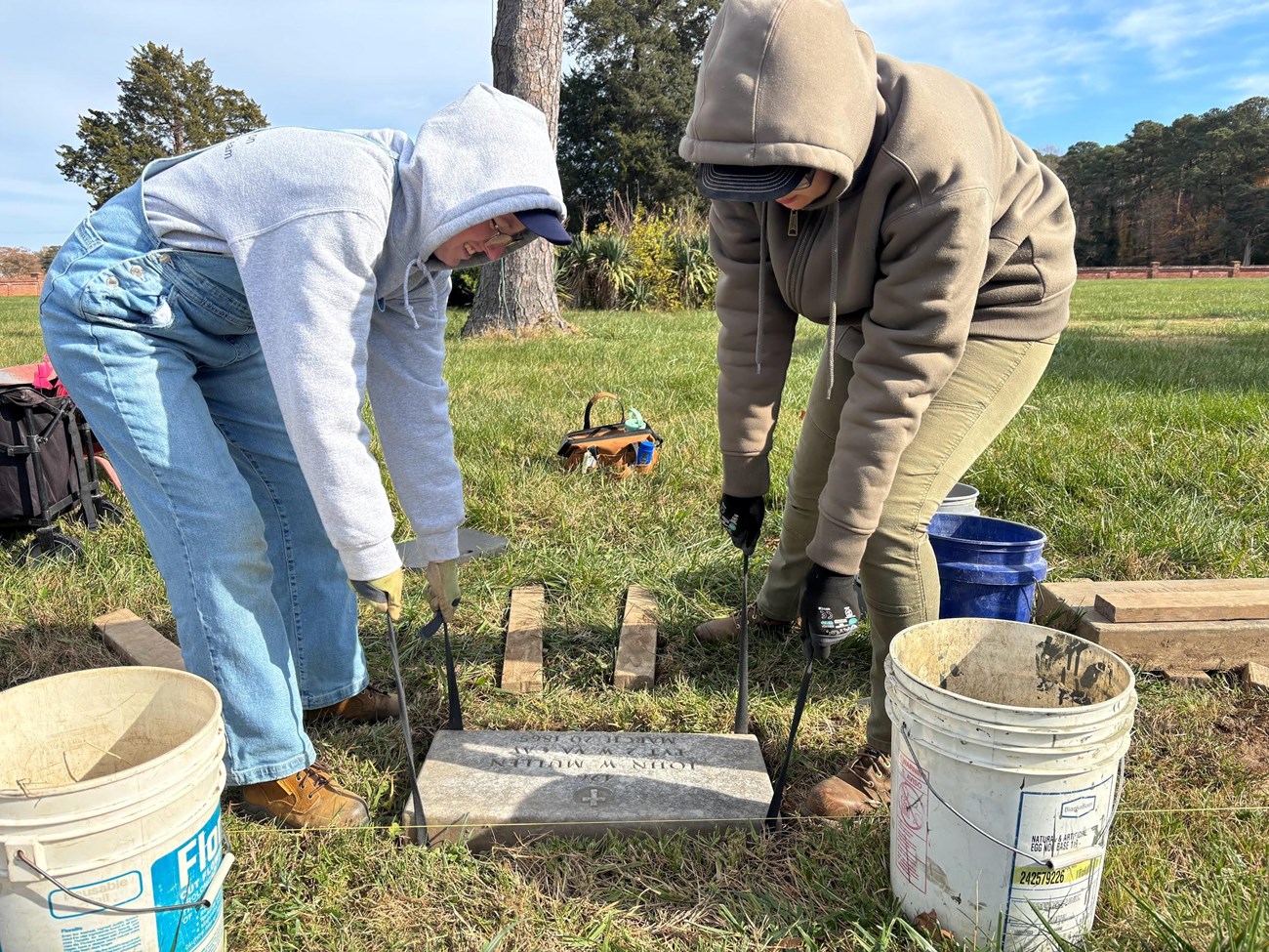 Two crew members lower a rectangular stone marker into a hole, even with the ground surface