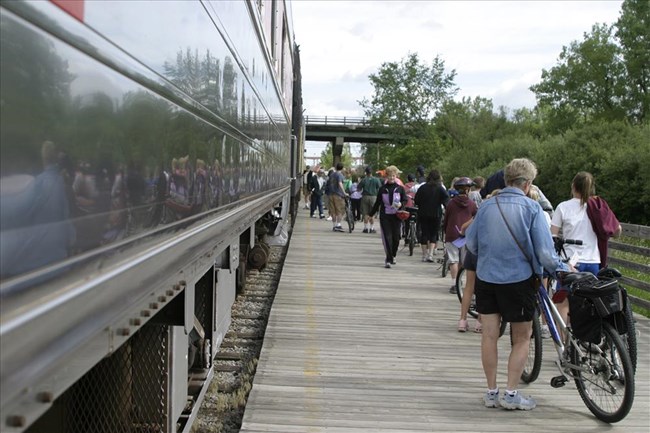 A line of people with bicycles stand on a wooden platform beside a train