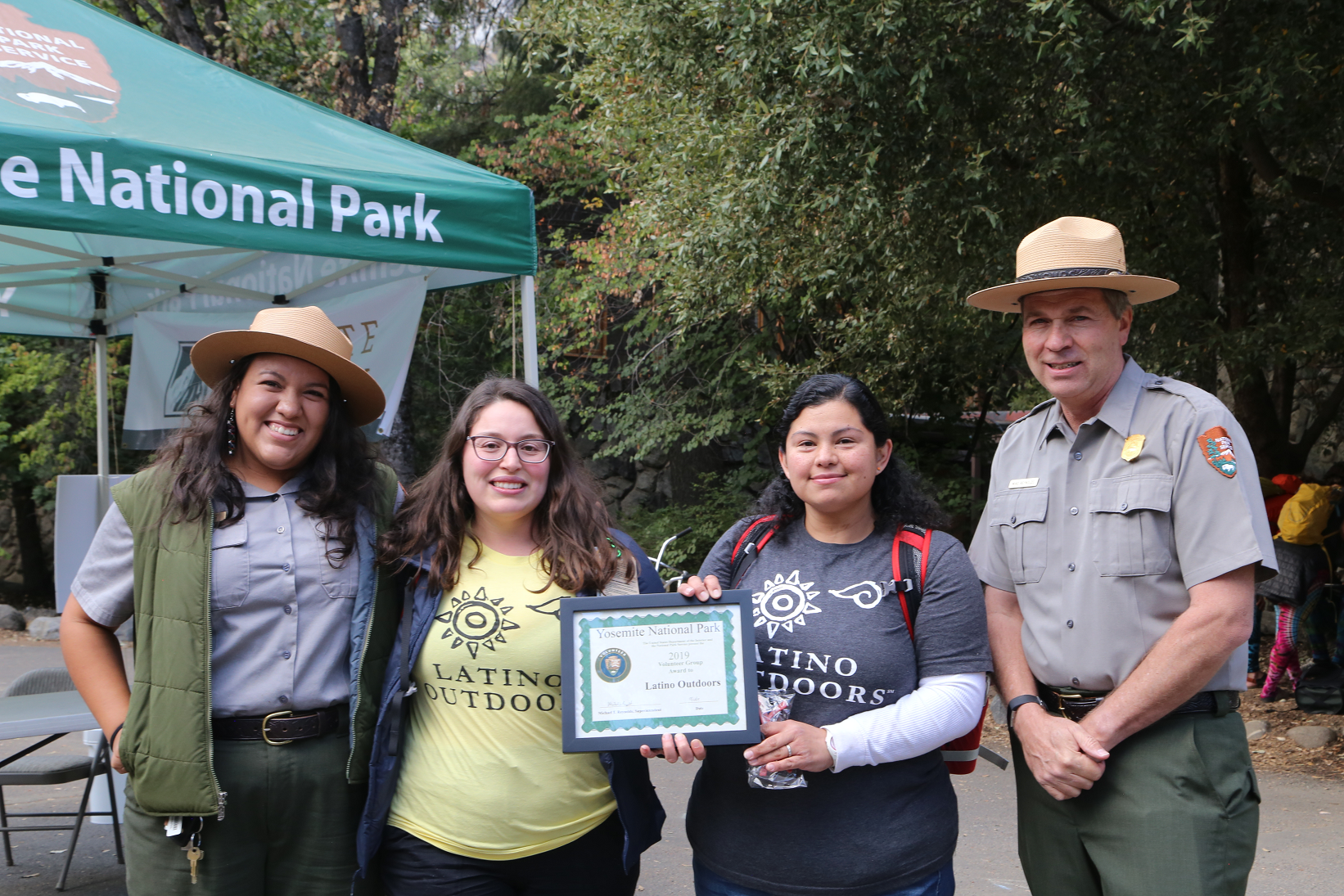 Latino Outdoors is awarded the 2019 Volunteer Group Award Two people with "Latino Outoors" shirts hold an award, standing between two NPS rangers in uniform, including Sandy Hernandez.
