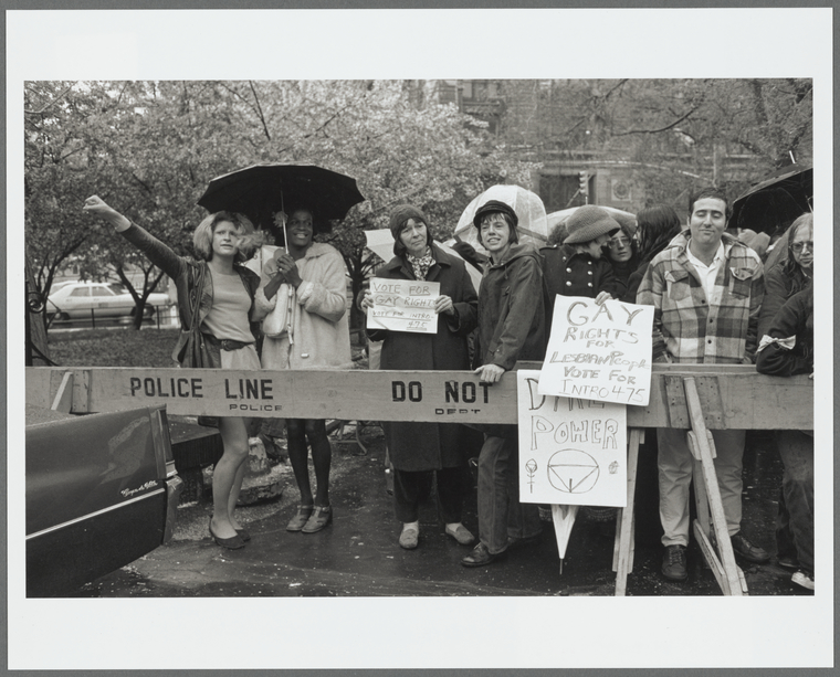 Gay rights activists at City Hall rally, standing with signs and umbrellas behind a barricade. L-to-R: Sylvia Ray Rivera, Marsha Johnson, Barbara Deming, Kady.