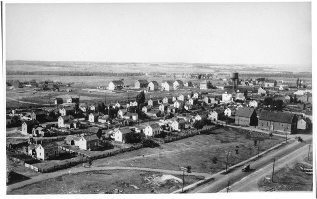 High angle view of a housing area on a grid of streets, with fenced yards and some larger buildings on the perimeter.