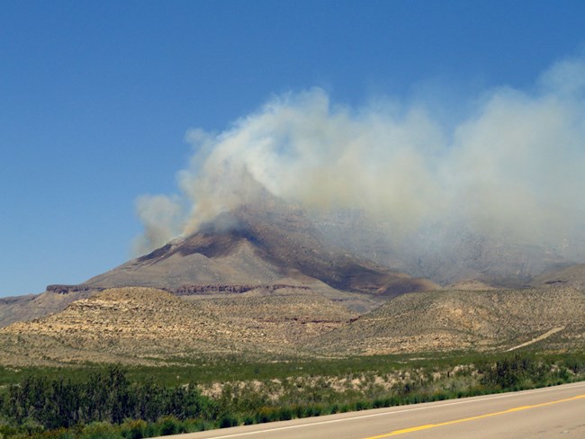 Smoke from El Capitan fire rises from a desert landscape.