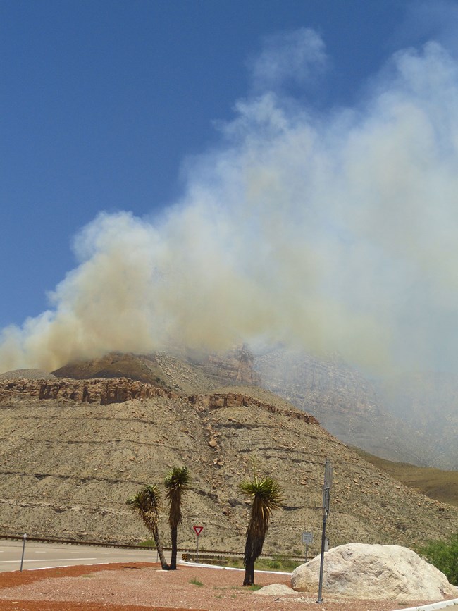 Smoke from El Capitan fire rises from a desert landscape.
