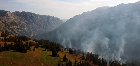 Mountainous terrain with smoke rising from forest in foreground.