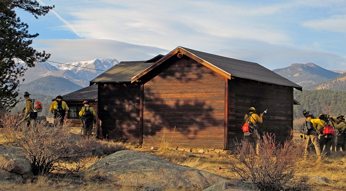 Fire crew works to remove vegetation from around the foundation of a wooden structure.