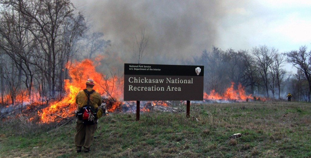 A firefighter monitors a prescribed fire near the park entrance sign