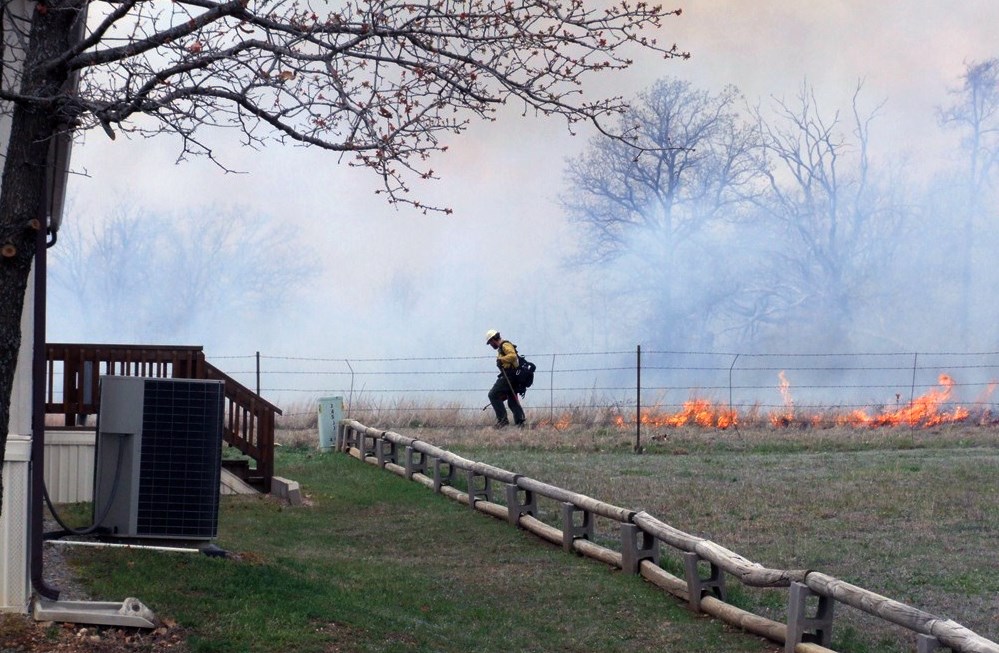 A firefighter uses a drip torch to ignite a prescribed fire along a fenceline.