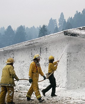 Two firefighters use a hose to spray foam on a dormitory structure