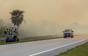 lt= A buggy and firefighters monitor on the side of a road while a truck is on the nearby road.