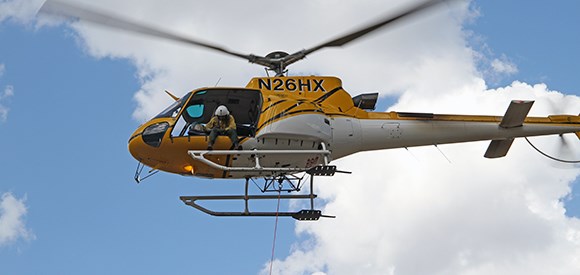 A spotter looks out the door from a helicopter.