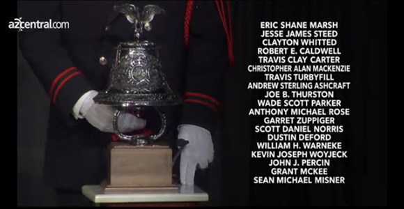 lt= A silver bell with a member of the military honor guard standing behind.