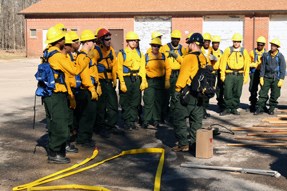 A group of firefighters gathered, listening to an instructor.
