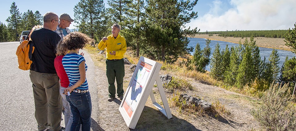 A man in Nomex near an information board talks to a group of visitors.