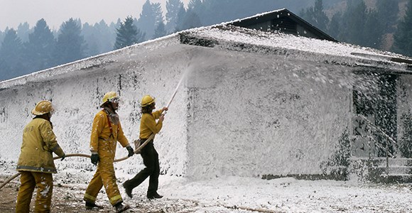 firefighters use a hose to spray foam on a dormitory structure