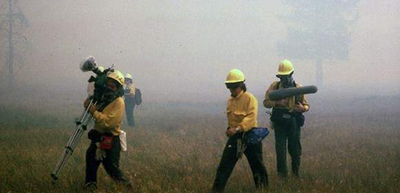 Film crew carrying equipment in dense smoke.
