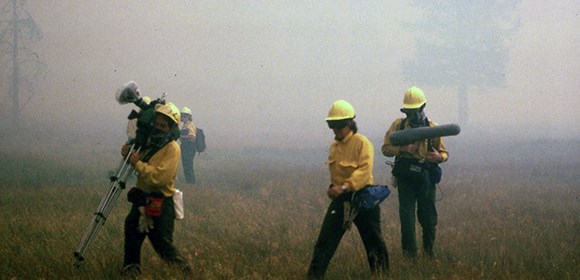 lt= Film crew carrying equipment in dense smoke.