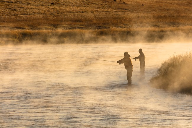 Two people fish in a steamy river early in the morning