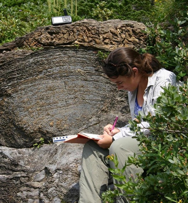 Photo of a person sitting by a rock outcrop.