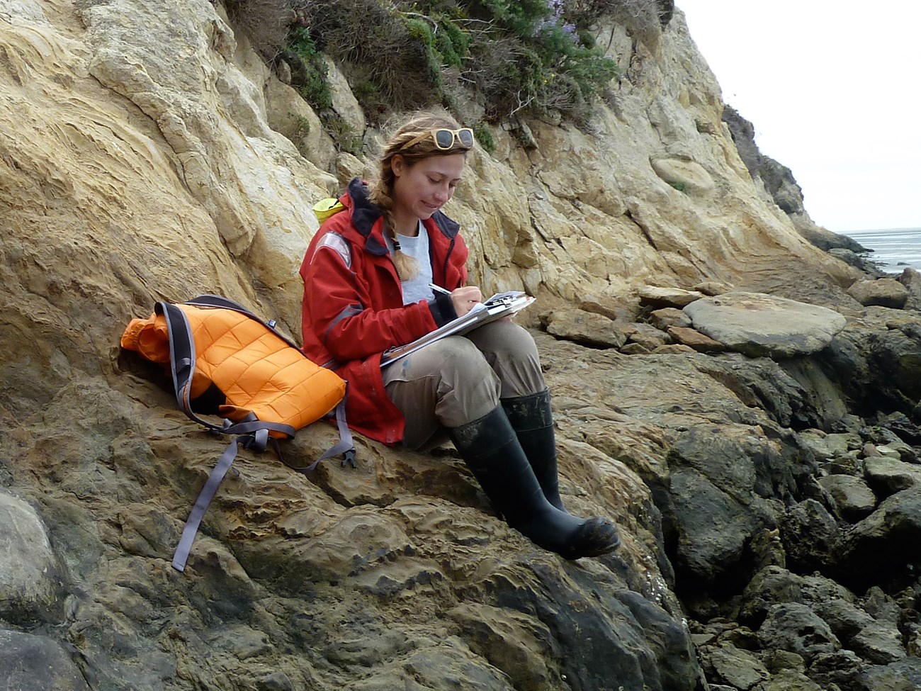 a person sitting on a shoreline bluff writing in a notebook