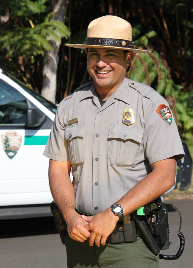 photo of a smiling park ranger standing with park vehicle in background