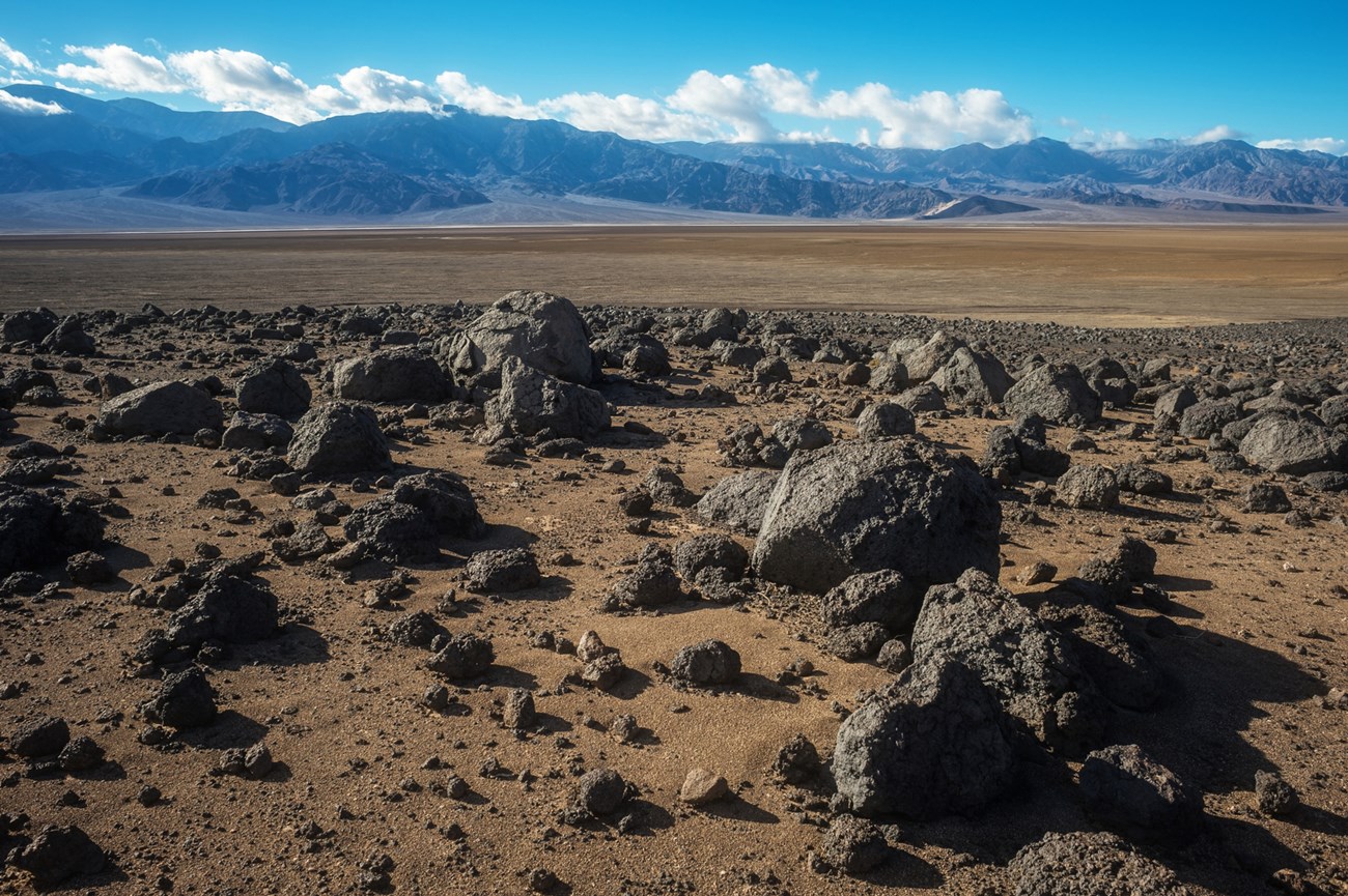 Black boulders over a brown plain, with distant mountains and blue sky.