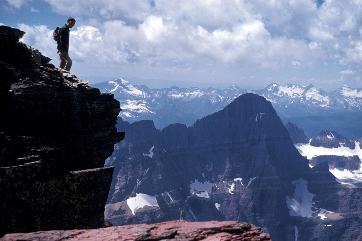 Photo of a person standing on a rock looking over a steep valley at a jagged peak.