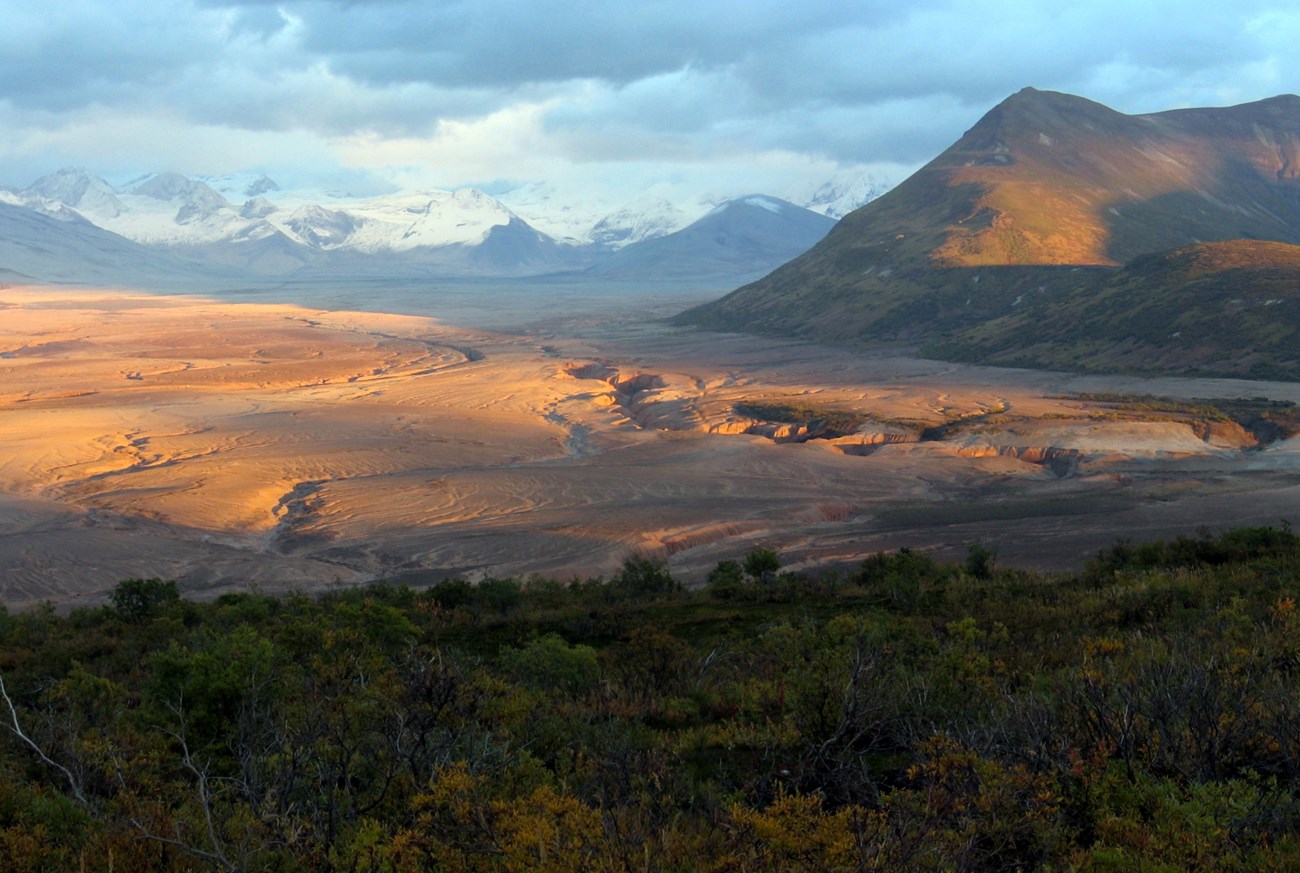 large valley with barren ground, tall mountains are visible in the distance