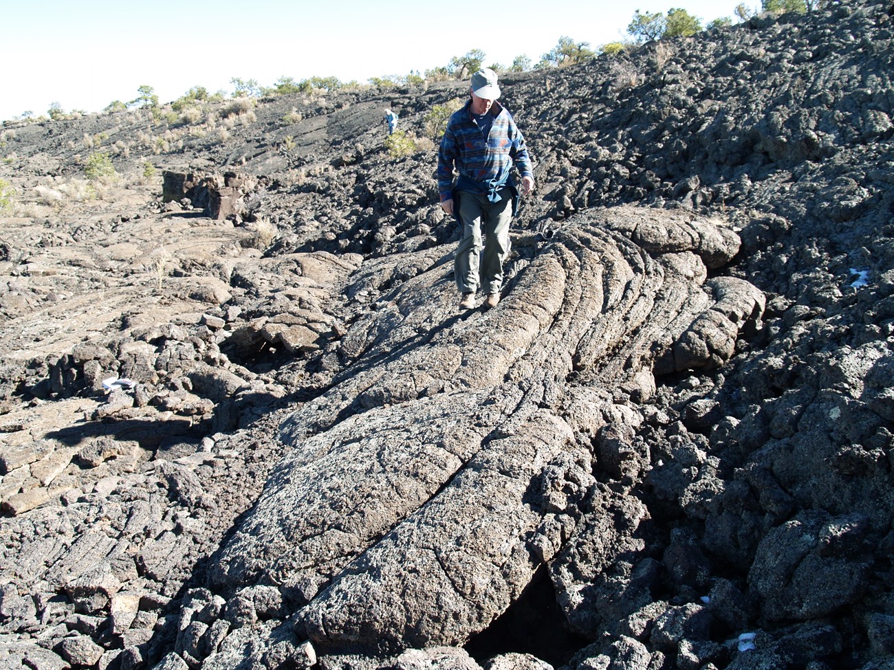 Photo of a person walking on lava rocks.