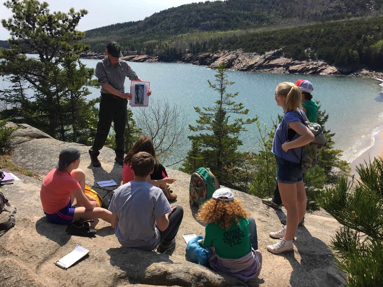 a ranger talking with students on a rocky overlook with ocean and beach below
