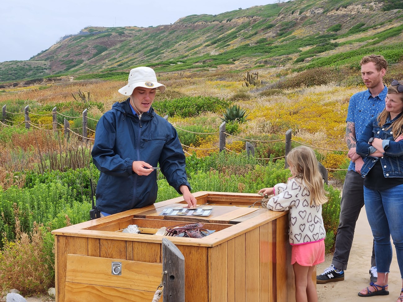 cabr tidepool education rocks and fossils A TPERP volunteer teaches a young girl and her parents about the tidepools’ rocks and fossils at the interactive Education Table. The wooden station stands out against the bright green native brush.