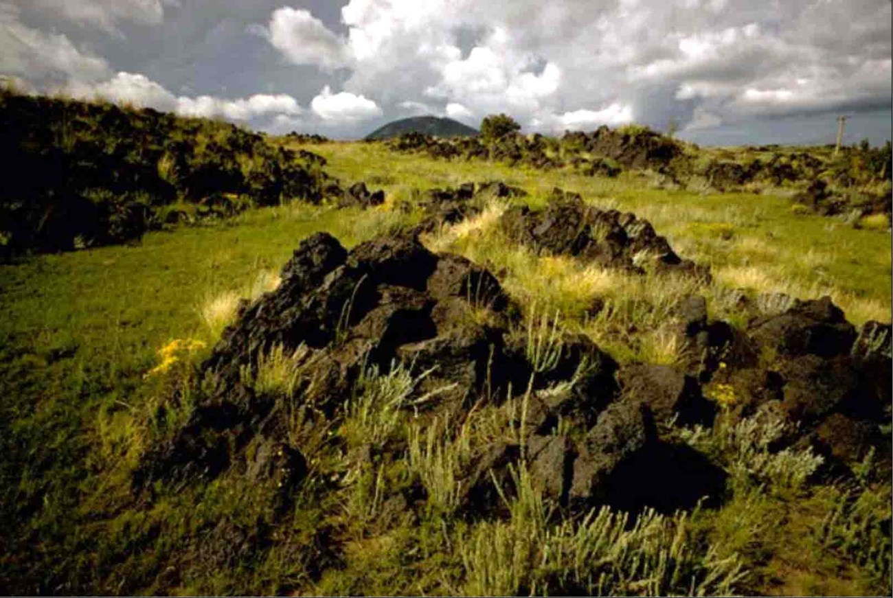 cavo basalt 2 Photo of a hill slope with dark rock outcrops and low vegetation.