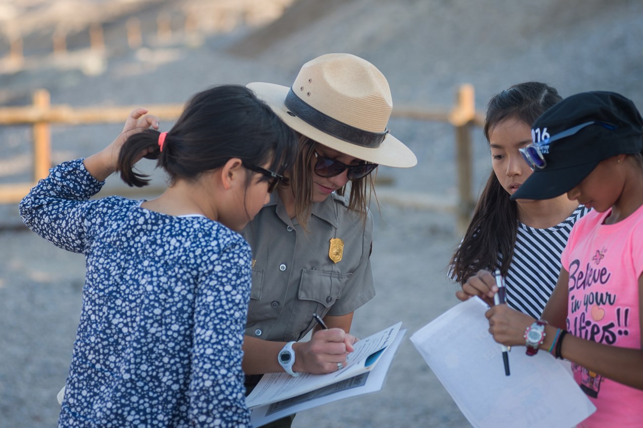 A park ranger writing in a booklet and surrounded by three young girls.