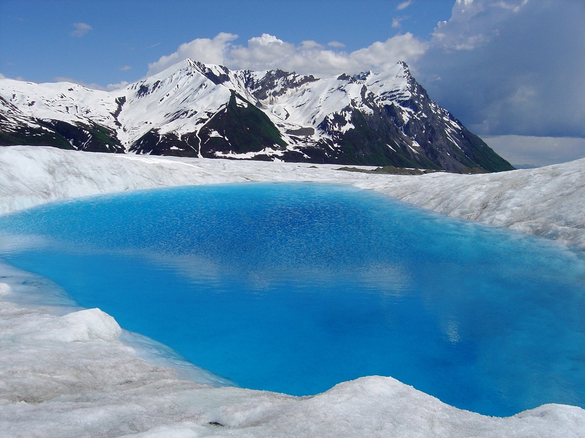 blue water pond on top of glacial ice with mountain in background