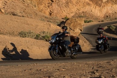 Three motorcyclists wearing helmets navigate turns on a desert road.