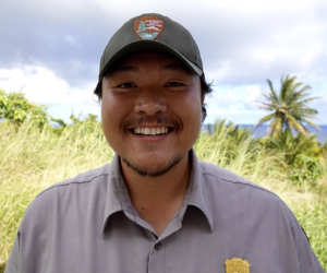 NPS staff member in uniform with grass and blue sky in background