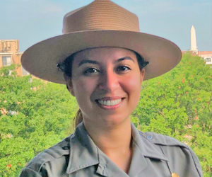 Learn more about Cynthia Hernandez. picture of woman posing in National Park Service Uniform with trees in background