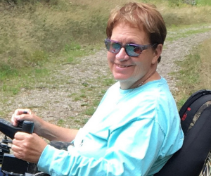 volunteer poses for photo in park while seated in a wheelchair