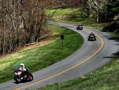 Three motorcyclists wearing helmets make their way around a curve and down a hill.