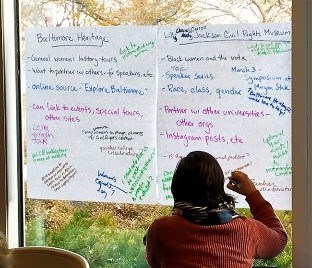 A woman in pink writes on two posters