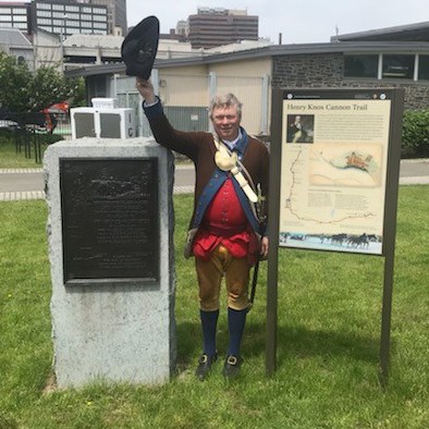 Historical reenactor Colonel James Johnson waves his hat between two Henry Knox Cannon Trail markers