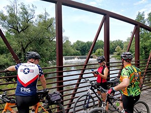 Three cyclists on a bridge looking at a waterfall.