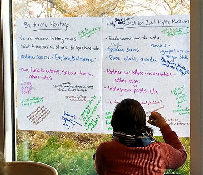 A woman writes ideas for improvement and collaboration on idea posters for Baltimore Heritage Area and the Lillie Jackson Civil Rights Museum.