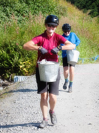 Two people carrying buckets full of rocks up a gravel path in the Mineshaft Grinder in Alaska