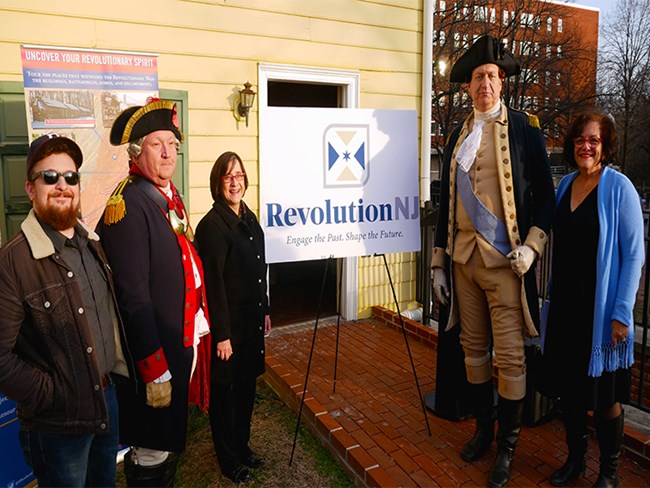 Five people stand with the new Revolution NJ logo on display.