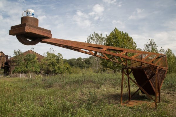 A rusted steel sculpture balances one ton of coking coal with a coffee mug.