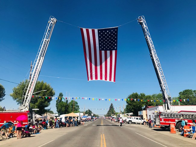 A large American flag hangs between two firetrucks for Pioneer Days in Manassa, CO