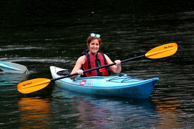 A woman smiles while floating in a kayak on a river.