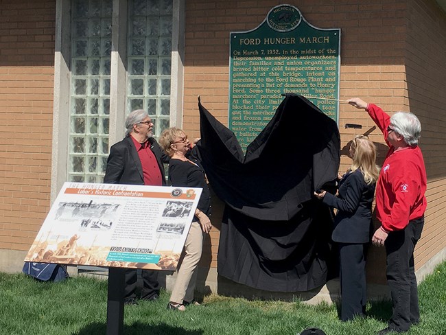 Four people unveiling new historic marker at UAW Local 600 in Dearborn, MI